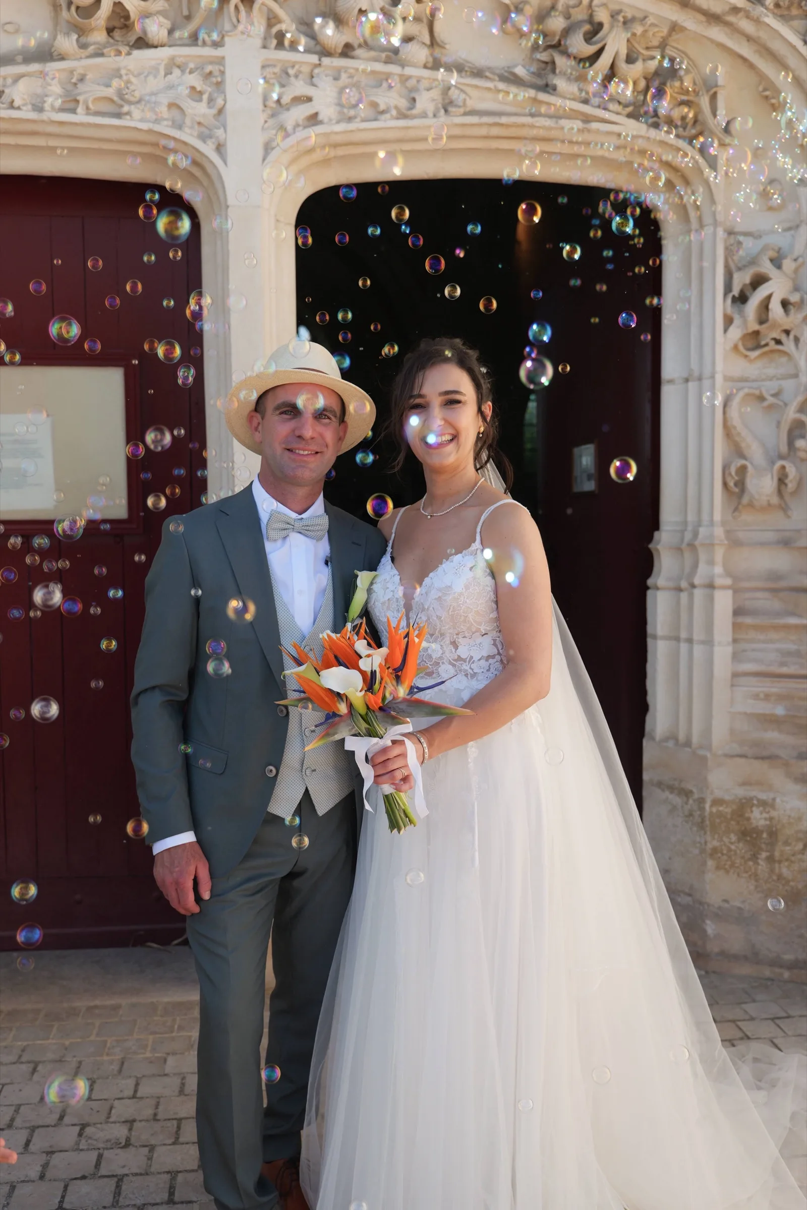 Les mariés devant une porte sculptée, bouquet orange à la main