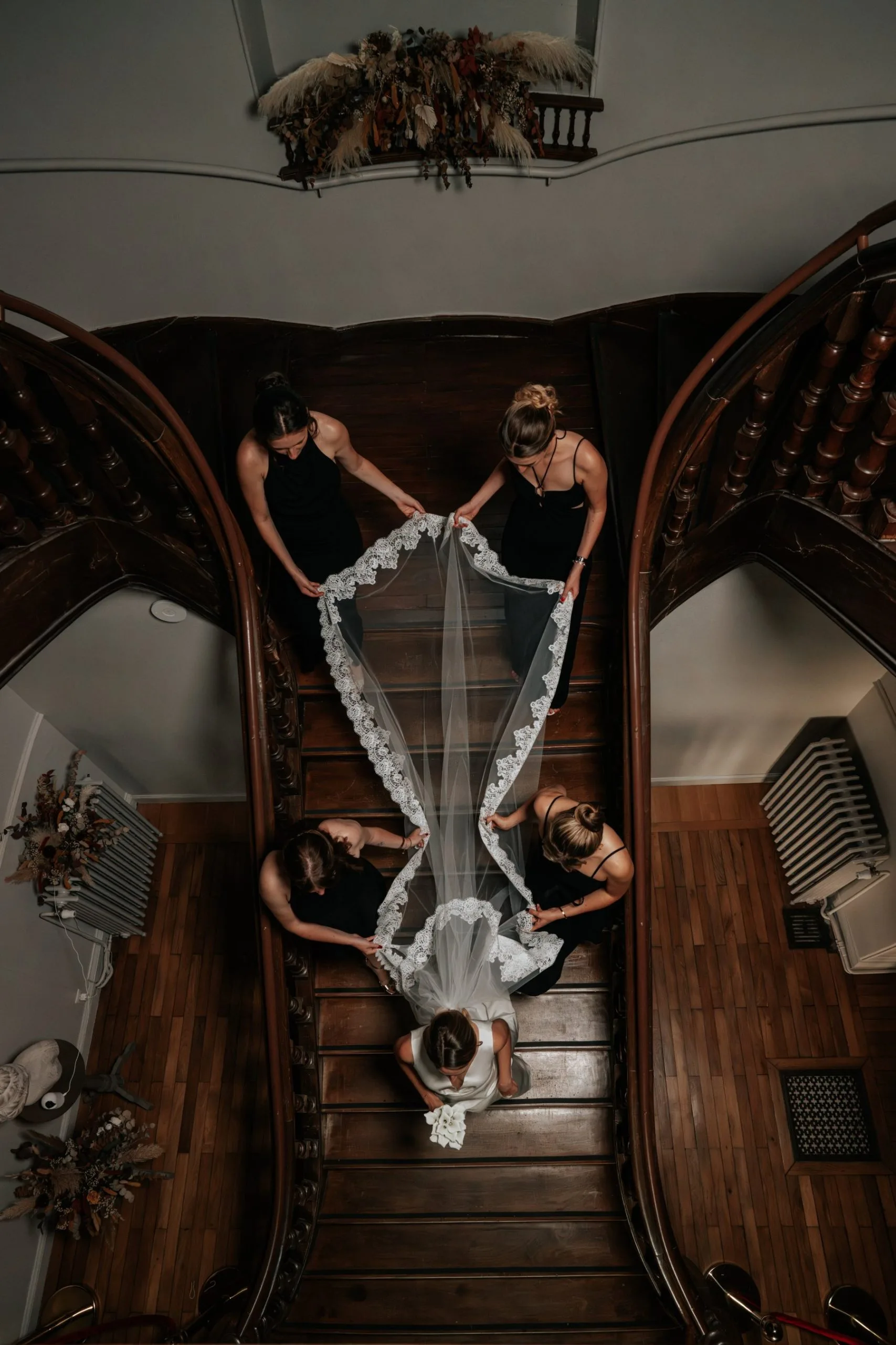 La mariée descend l’escalier, ses demoiselles d’honneur portent le voile