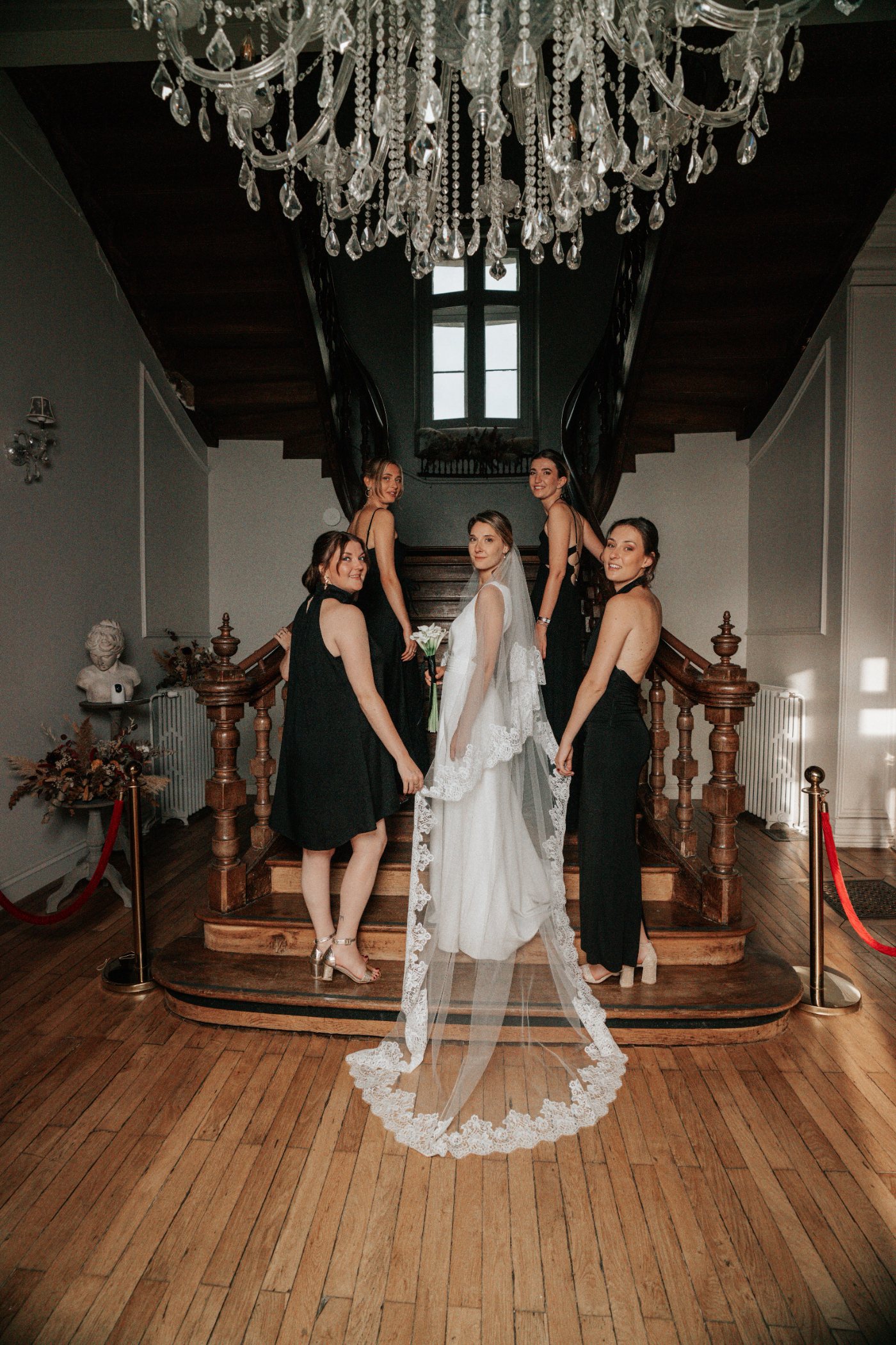 La mariée et ses demoiselles d’honneur sur le grand escalier, sous le lustre